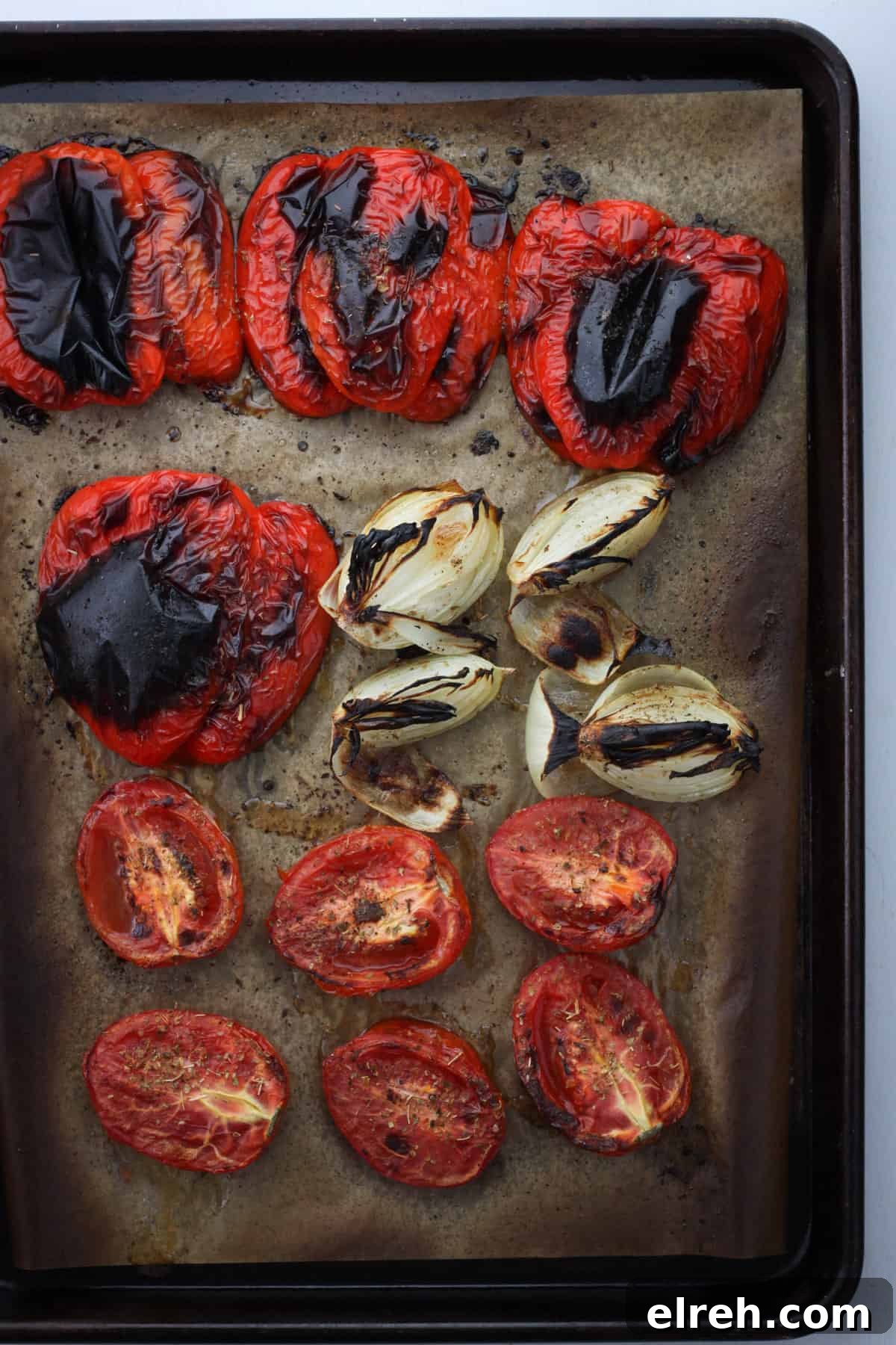 A sheet tray with roasted red peppers, charred onions and roasted Roma tomatoes.