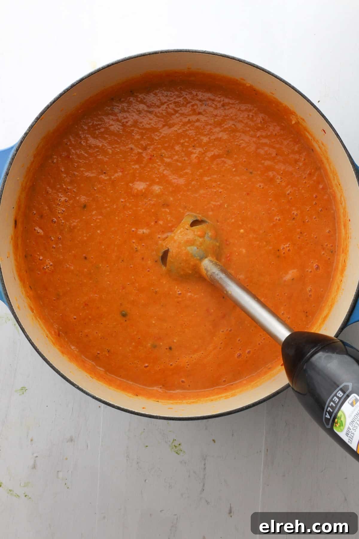 A Dutch oven with pureed lentil and red pepper with an immersion blender partially in the pot.