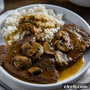 Two cooked steaks covered with gravy and mushrooms with a side of rice and gravy.