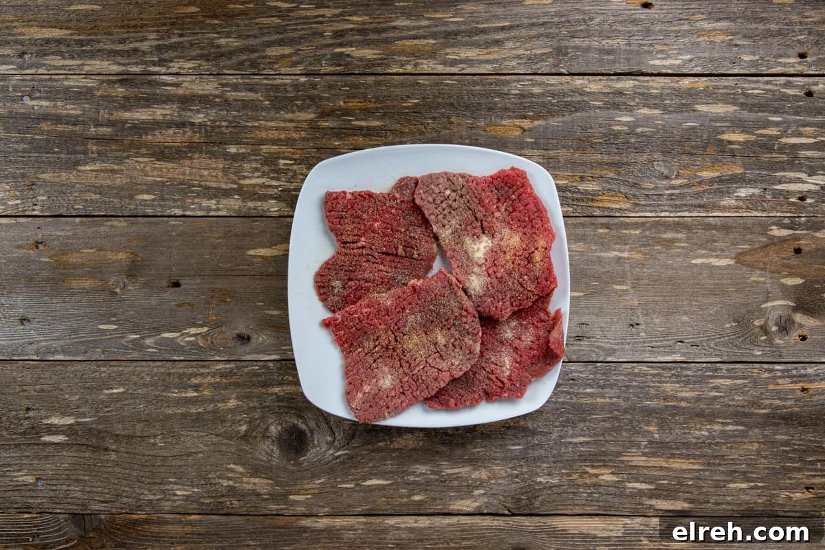 Raw seasoned minute steaks on square white plate.