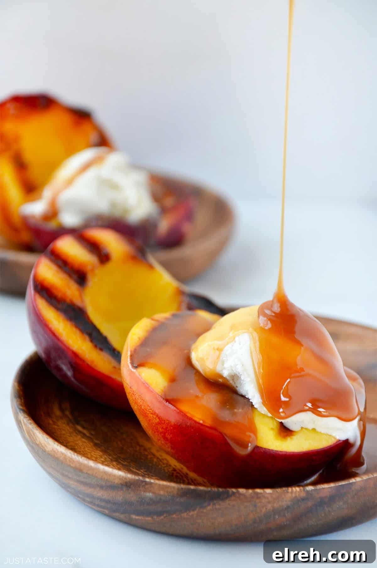 Grilled peaches with vanilla ice cream being drizzled with caramel sauce.