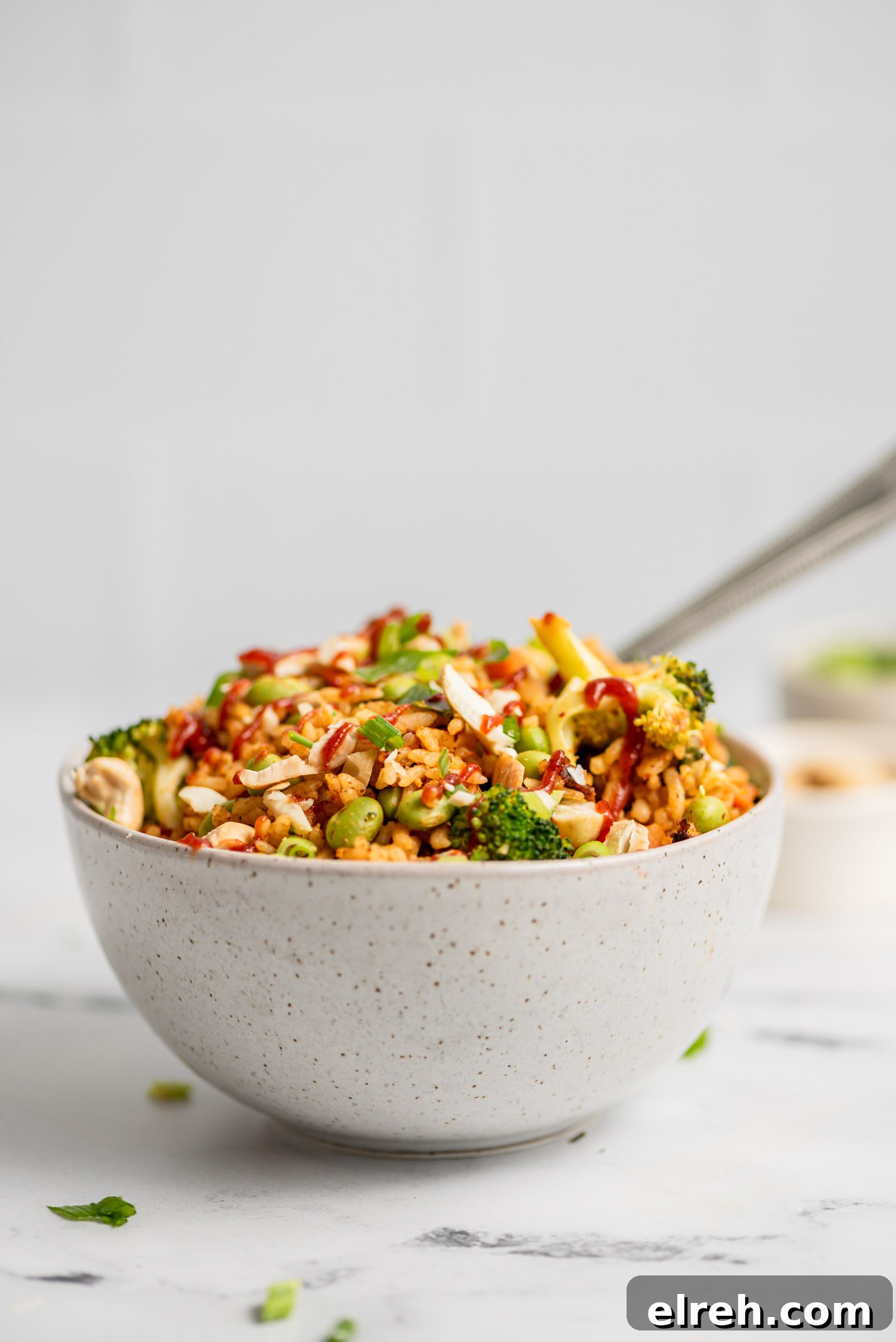 Bowl of fried rice with broccoli, carrot, edamame and green onion topped with chopped cashews.