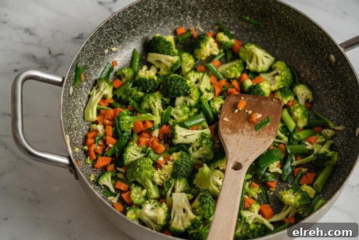 Broccoli, carrot, garlic and green onion cooking in a skillet.