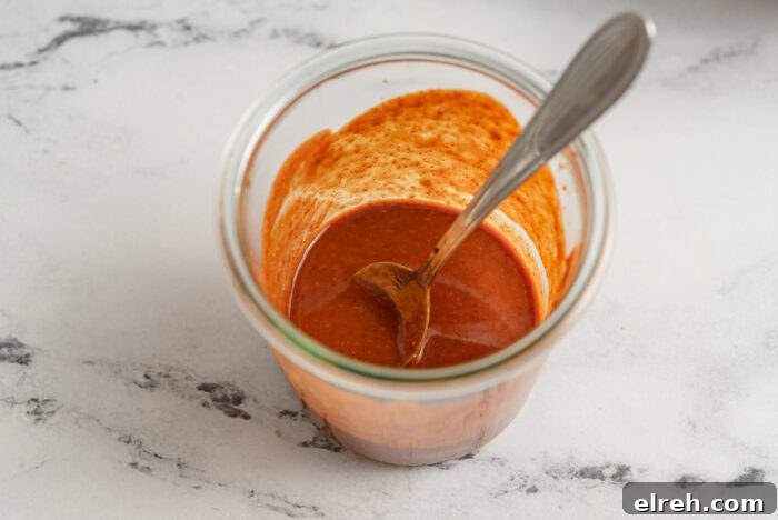 Red sauce in a glass jar with a spoon.