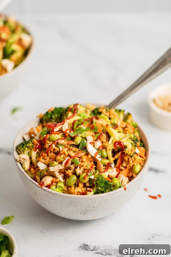 Bowl of fried rice with broccoli, carrot, edamame and green onion topped with chopped cashews.