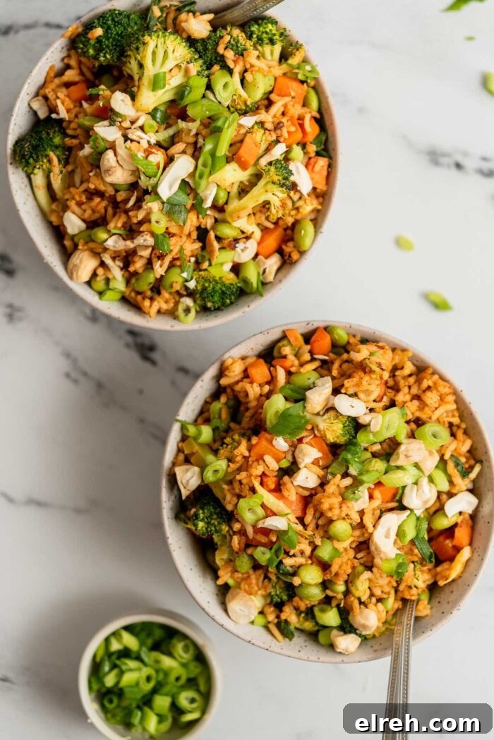 Two bowls of fried rice with broccoli, carrot, edamame and green onion topped with chopped cashews.