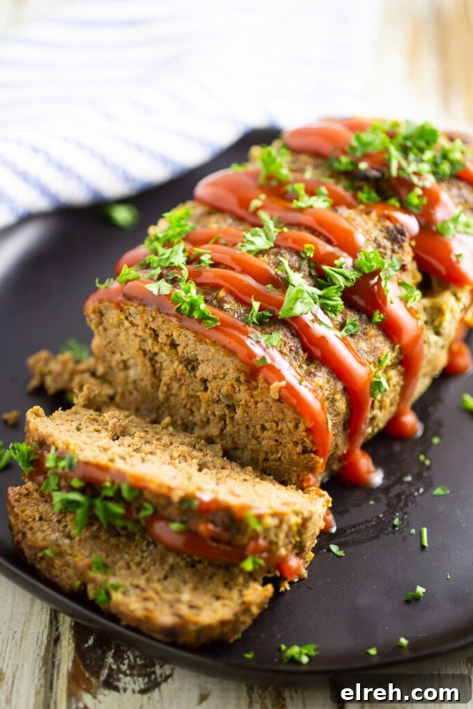 Full meatloaf on a large plate with 2 slices cut off garnished with ketchup drizzle and fresh chopped parsley.