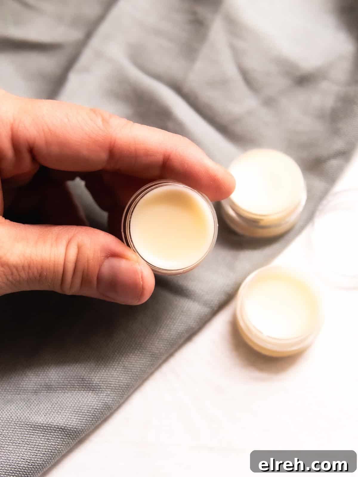 How to Make Tallow Lip Balm for Soft, Hydrated Lips 8 Holding a container of tallow lip balm with more containers in the background.