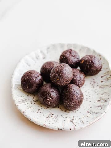 Eight small chocolate date balls on a small speckled white plate.