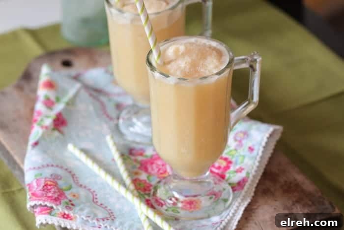 Refreshing Summer Drink Recipes to Beat the Heat 5 Two side-by-side honey and orange creamsicle slushies on a floral cloth, with straws.