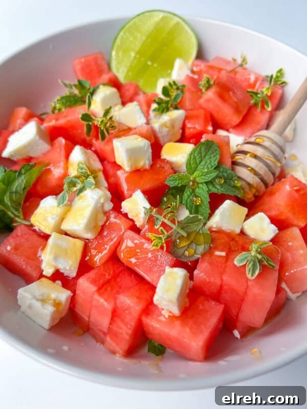 A vibrant bowl of Watermelon Feta Salad, featuring cubed watermelon and feta cheese, garnished with fresh mint and herbs.