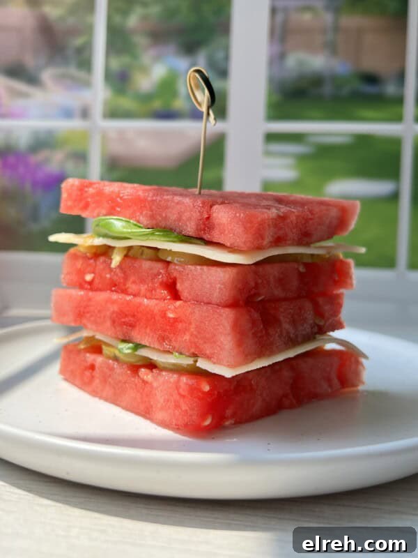 Watermelon Sandwich Recipe for a Refreshing Summer Snack 7 A stack of square watermelon slices layered with cheese and greens, held together by a toothpick, sits on a white plate with a sunlit garden visible through a window in the background.
