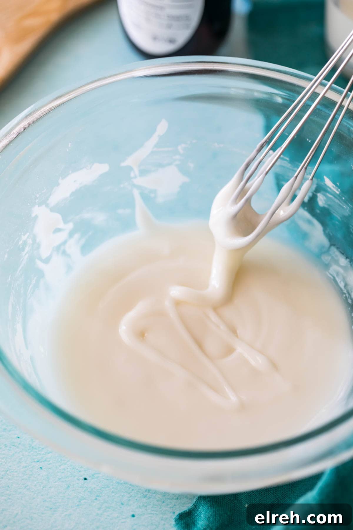 whisk lifting out of a thin glaze in a glass bowl