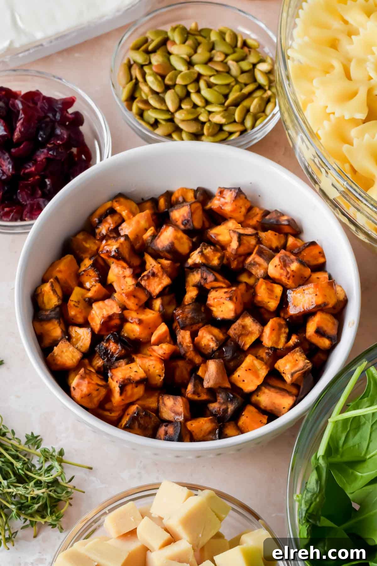 Fall Pasta Salad with Roasted Butternut, Cranberries and Feta 4 roasted sweet potato cubes in white bowl surrounded by additional ingredients for fall pasta salad.