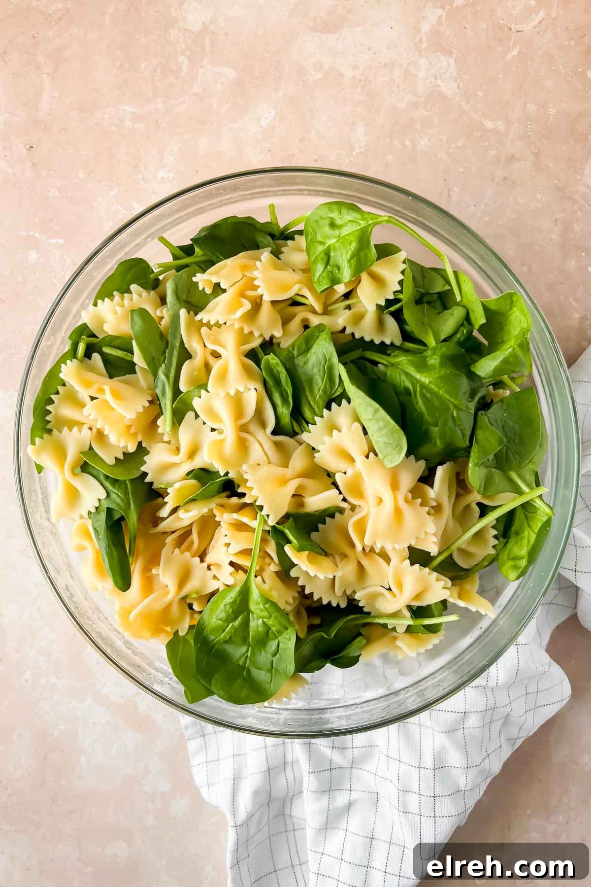 Fall Pasta Salad with Roasted Butternut, Cranberries and Feta 6 bowtie noodles and spinach in glass mixing bowl.