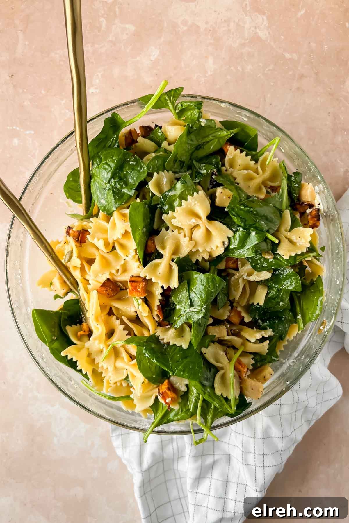 Fall Pasta Salad with Roasted Butternut, Cranberries and Feta 9 tossed noodles, spinach and sweet potatoes in glass mixing bowl with two gold spoons.
