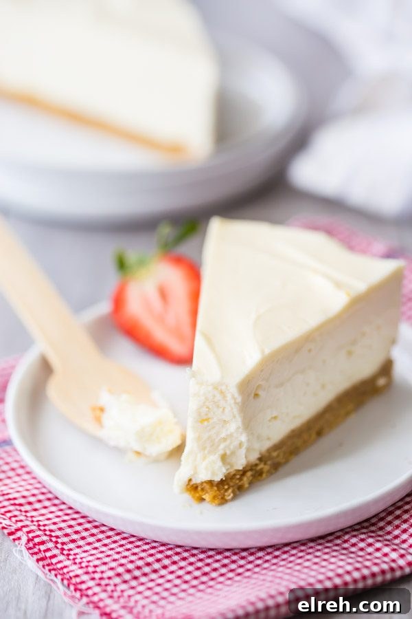 slice of no bake cheesecake with a bite out of it on a white plate with a wooden spoon and a strawberry. sitting on a white and pink checked napkin