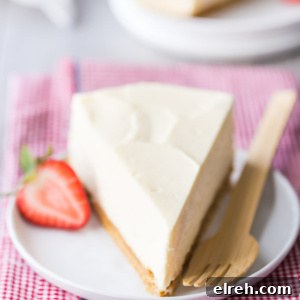 No-Bake Cheesecake slice on a white plate with a fork and half strawberry sitting on a pink/white checked napkin. another slice in view in the background