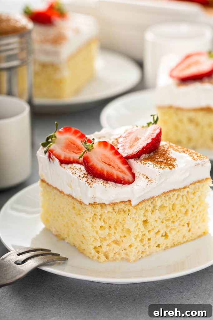 moist tres leches cake on plate with frosting and strawberry halves