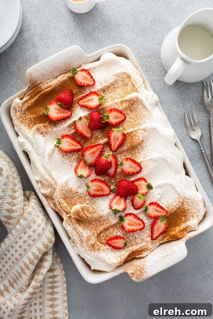Cake topped with whipped cream frosting, dusted with cinnamon and garnished with strawberries in a rectangular cake pan