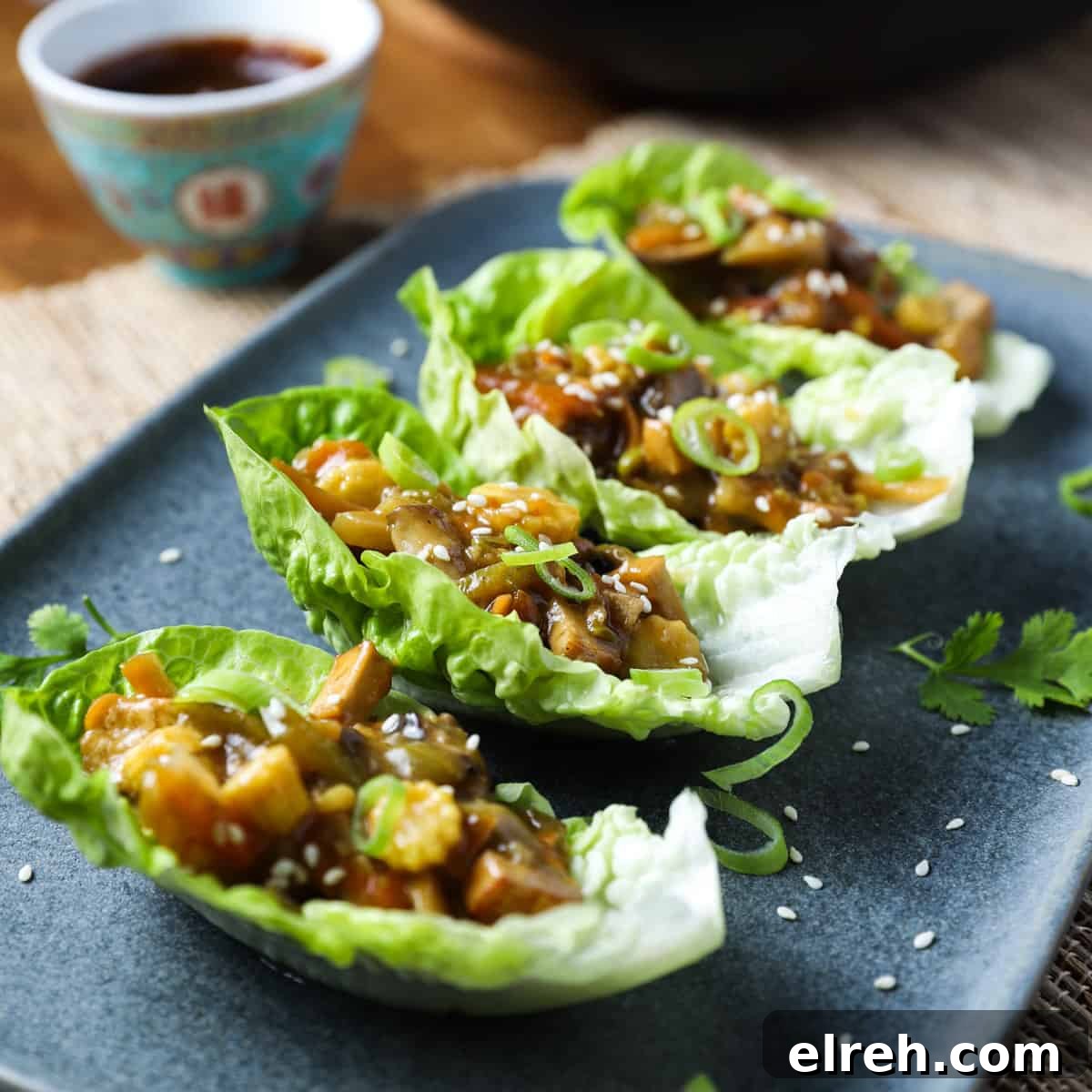 Vegan San Choy Bau Lettuce Cups 13 Photo of 4 lettuce leaves with vegan san choy bau filling inside, placed on a blue-grey oblong plate with a chinese dish of hoisin sauce to the side.