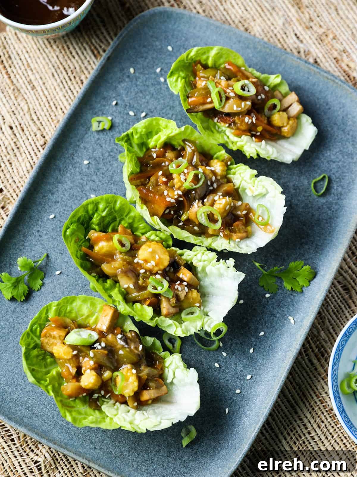 Vegan San Choy Bau Lettuce Cups 3 Overhead photo of vegan san choy bau in lettuce leaves on a blue-grey oblong plate on a jute mat underneath.