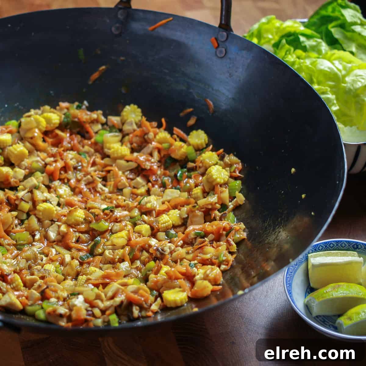 Vegan San Choy Bau Lettuce Cups 4 Photo of vegan san choy bau filling cooked in a wok, with a plate of lettuce leaves to the side and some lime wedges.