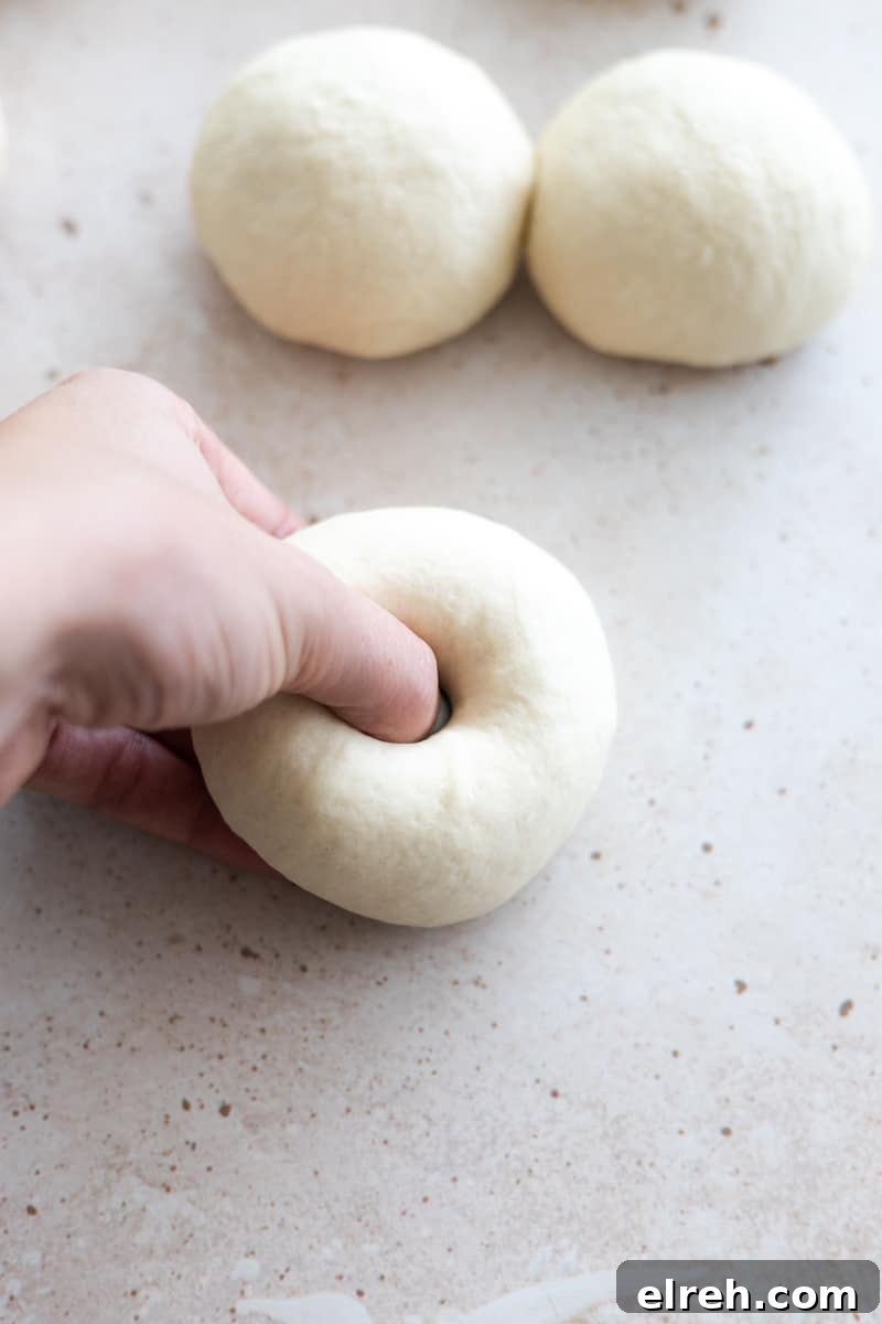 A thumb pressing a hole in the center of the dough ball to shape the bagel. 