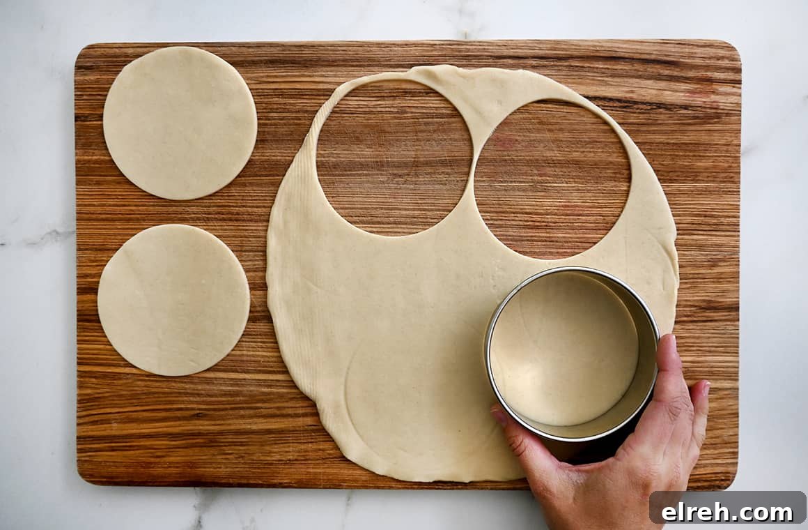 A hand holding a round cookie cutter stamps out round dough circles