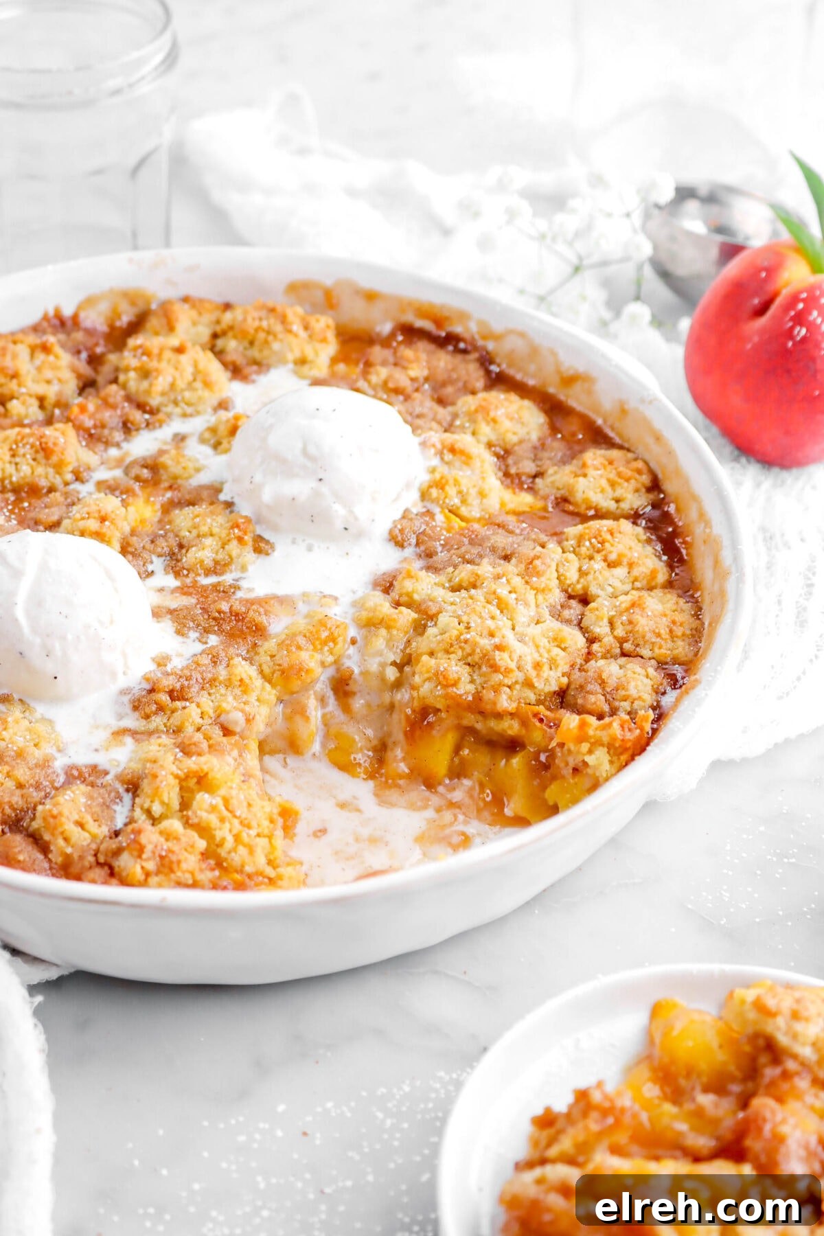 Peach Cobbler Crisp with Brown Sugar and Cinnamon 3 angled shot of peach cobbler with some missing with melting ice cream on top in white casserole.