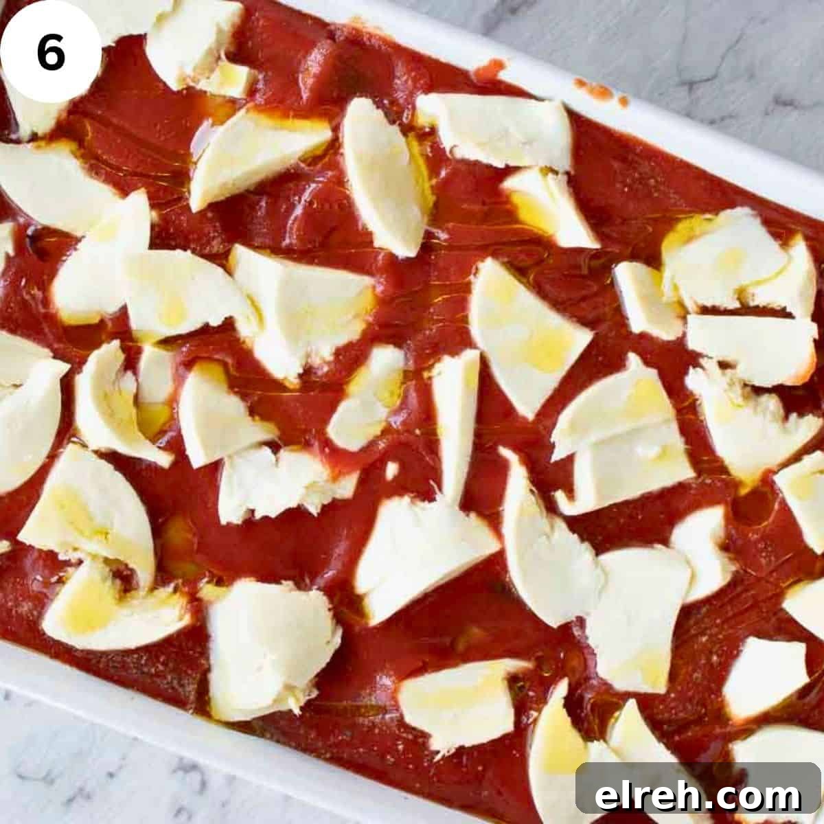 Overhead view of tomato puree in a baking dish topped with chopped cheese.