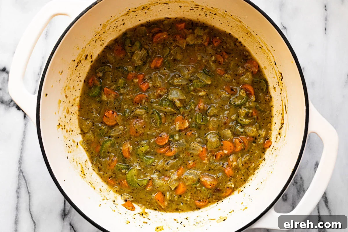 Sauteed veggies and broth in a large white pot.