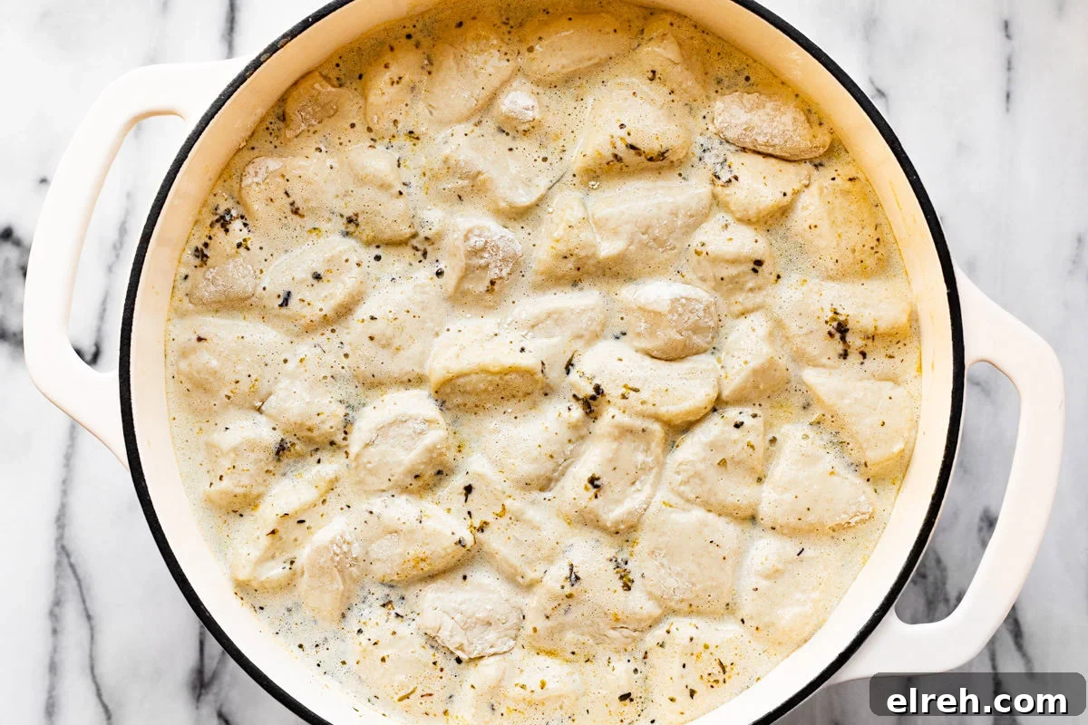 Chopped biscuit dough in a large pot of chicken dumpling soup.