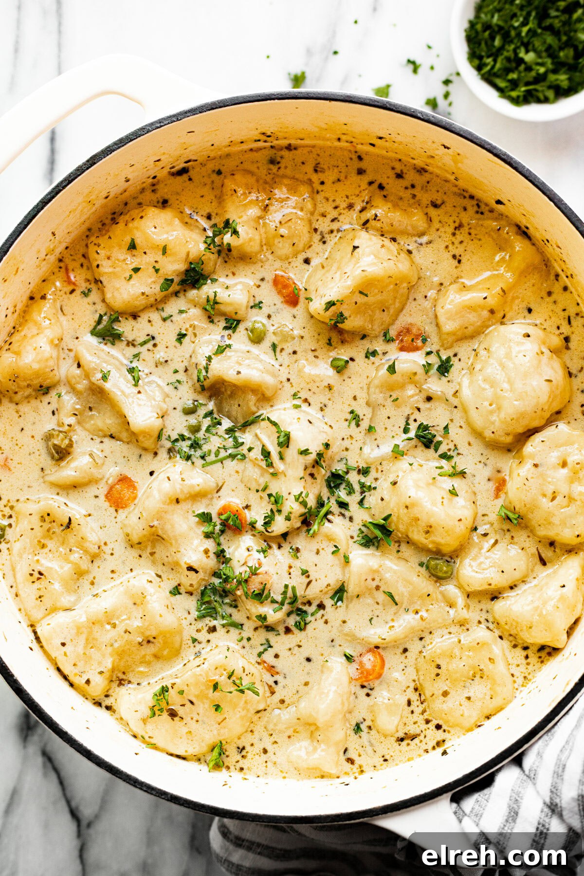 White pot filled with homemade chicken dumpling soup garnished with parsley.