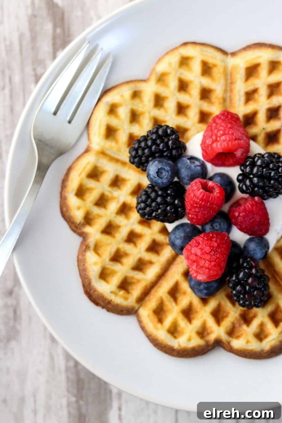 Heart-shaped waffle on a plate topped with whipped cream and fruit.