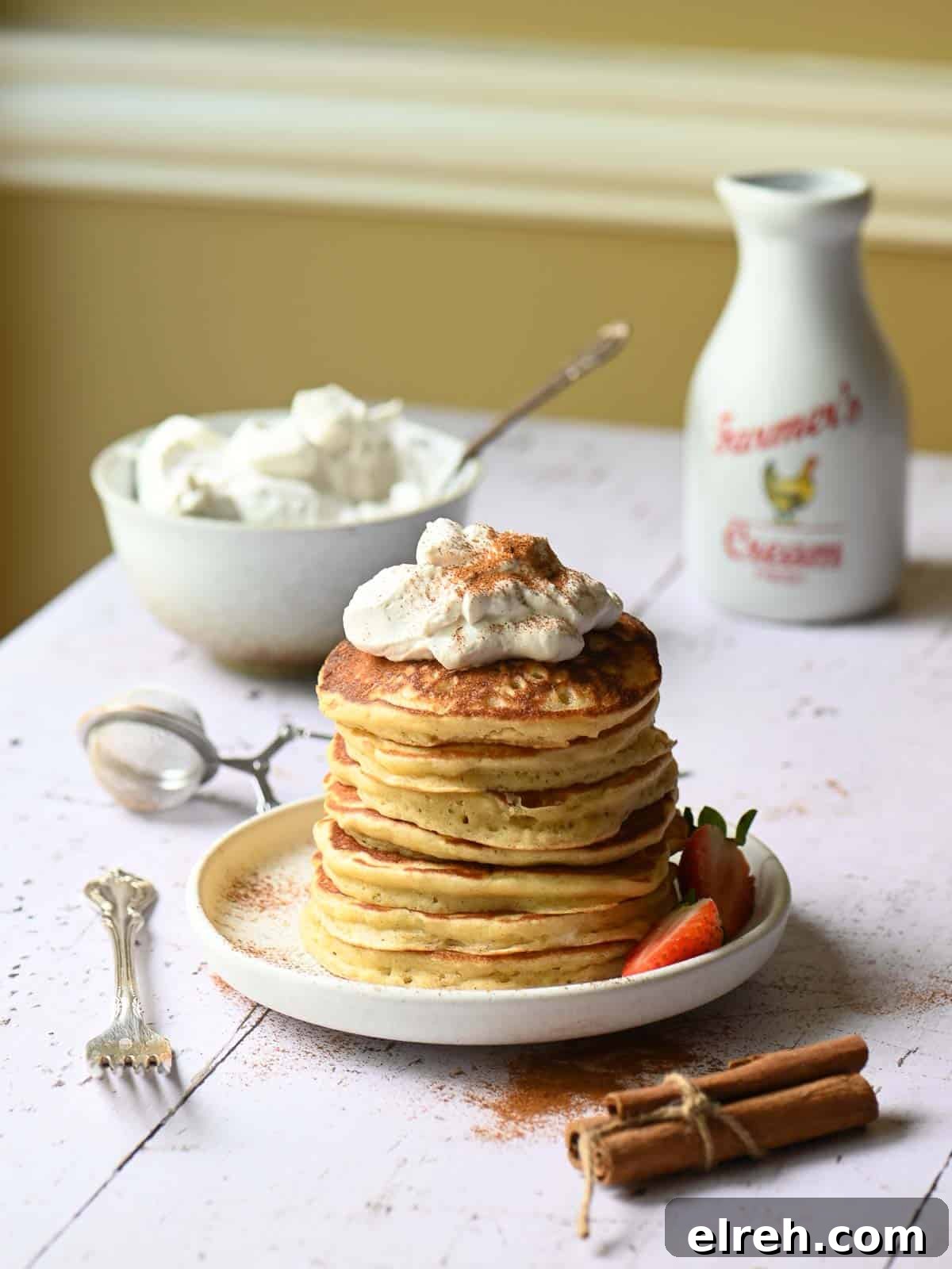 Fluffy Sweet Cream Cinnamon Pancakes Recipe 2 A stack of cinnamon pancakes with whipped cream on top on a white board.