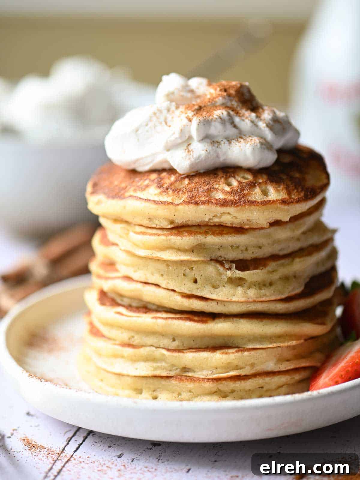 Fluffy Sweet Cream Cinnamon Pancakes Recipe 3 Close up of a stack of pancakes with whipped cream on top and cinnamon.