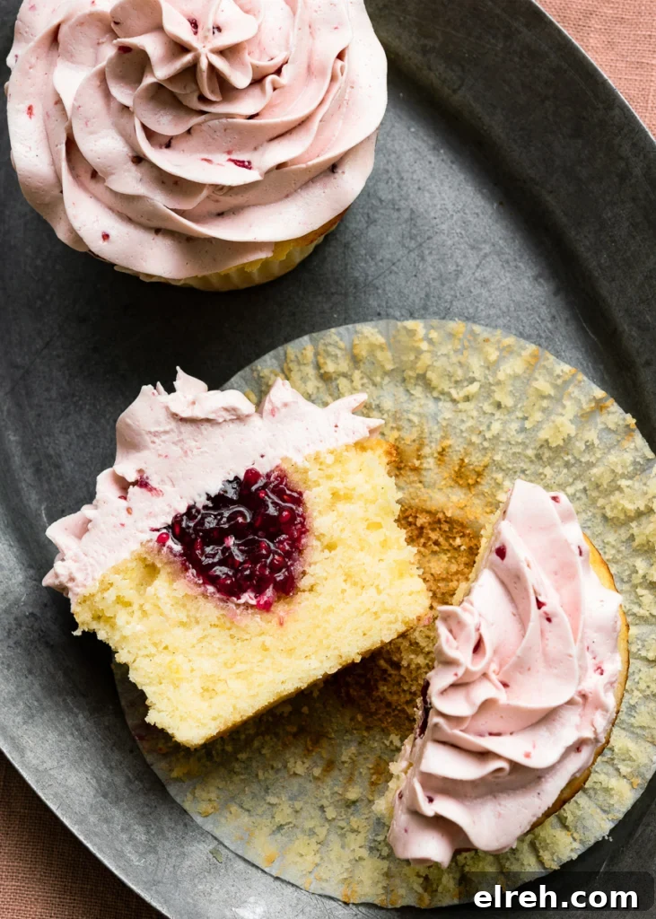 Lemon Raspberry Cupcake Recipe with Zesty Lemon Frosting 3 Sliced lemon cupcake with raspberry jam filling and raspberry icing laying cut side open on a plate.