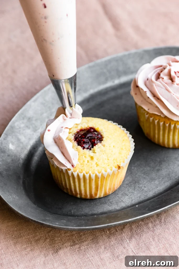 Lemon Raspberry Cupcake Recipe with Zesty Lemon Frosting 4 Piping bag starting to frost buttercream onto the top of a raspberry jam center filled cupcake.