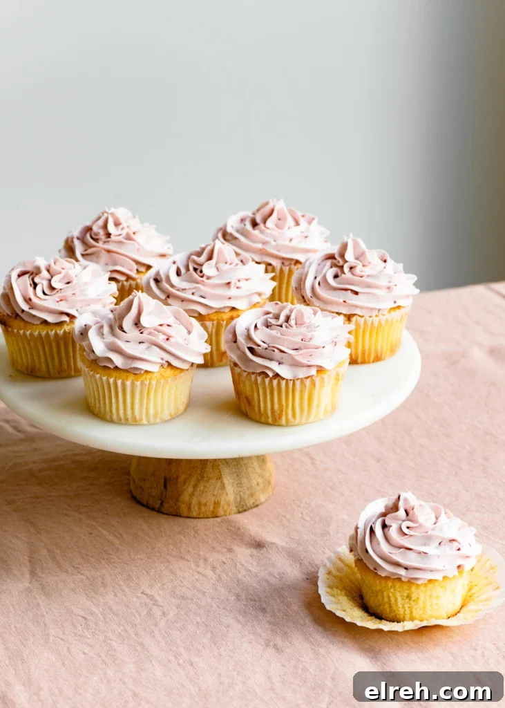Lemon Raspberry Cupcake Recipe with Zesty Lemon Frosting 5 Cake stand full of raspberry frosting topped lemon cupcakes on a linen covered table.