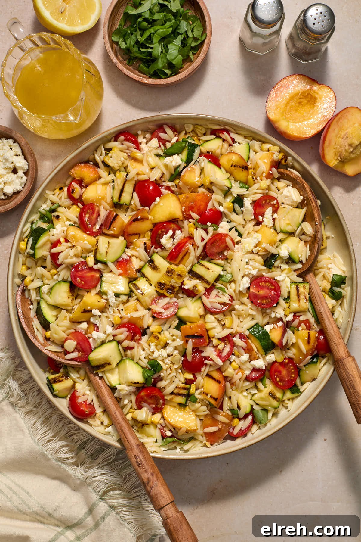 Grilled Vegetable Orzo Salad with Summer Peaches 2 Vegetable orzo salad assembled in a bowl with serving spoons and extra vinaigrette and chopped basil on the side.