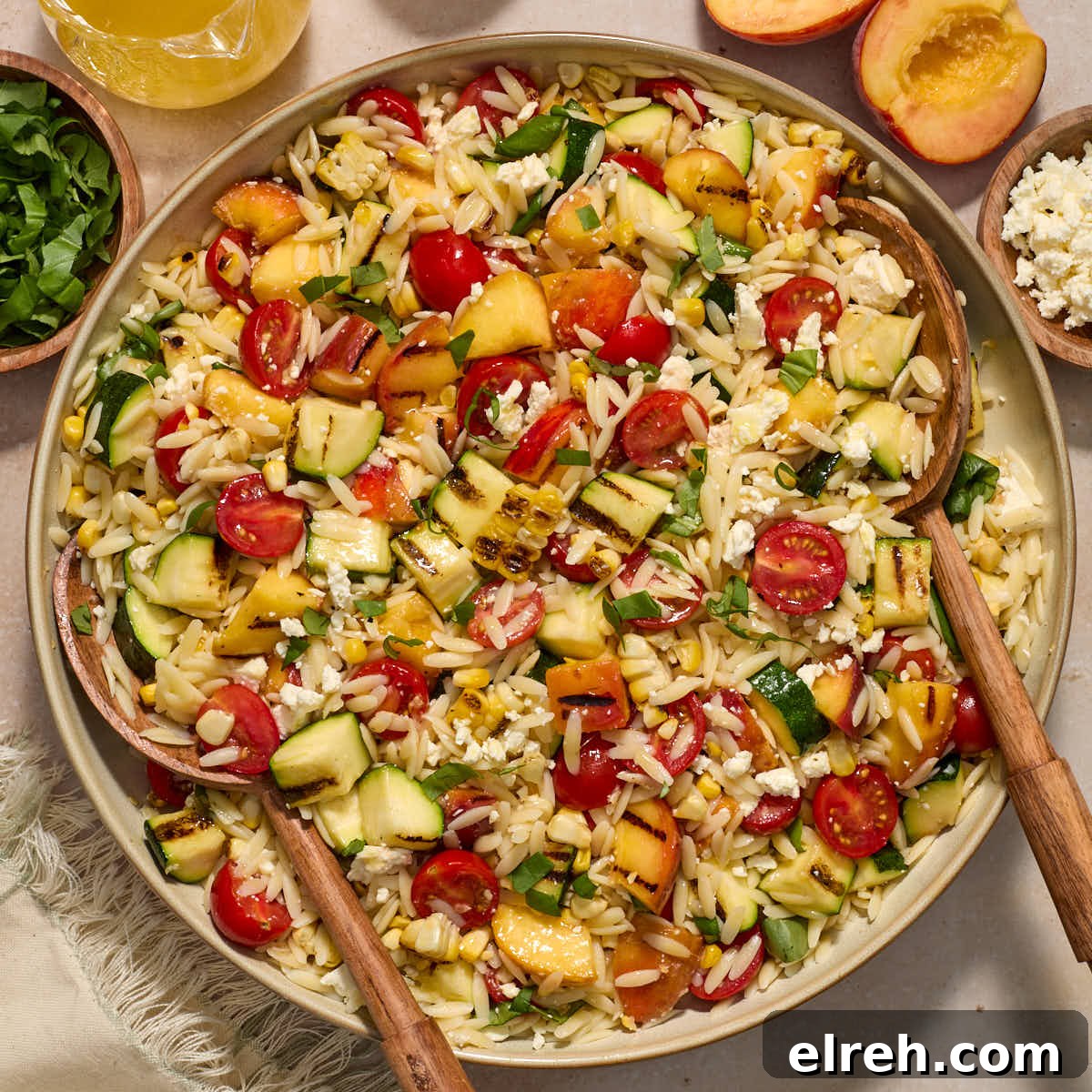 Grilled Vegetable Orzo Salad with Summer Peaches 11 Grilled summer vegetable orzo salad served in a large bowl with serving spoons inserted into it.