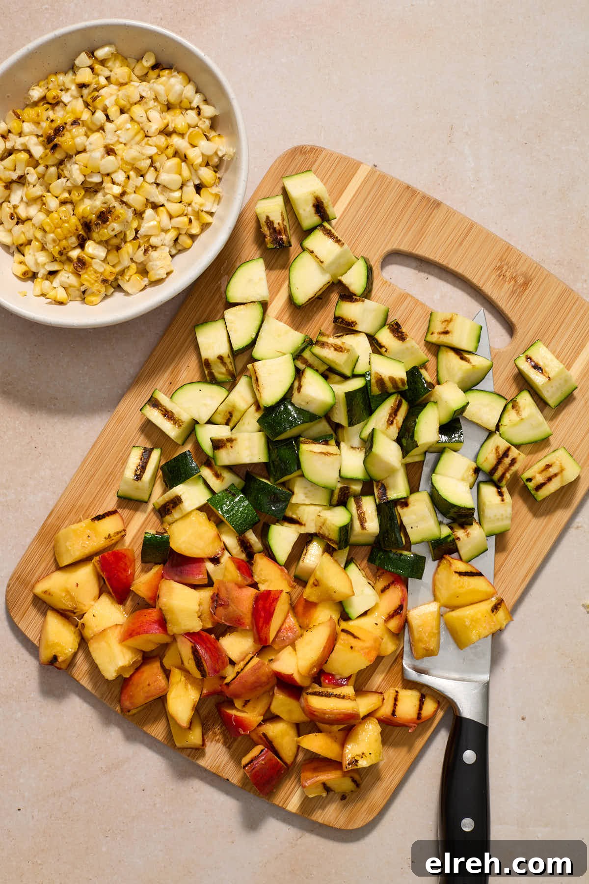 Grilled Vegetable Orzo Salad with Summer Peaches 8 Chopped zucchini and peaches on a wooden board with a bowl of corn on the side.