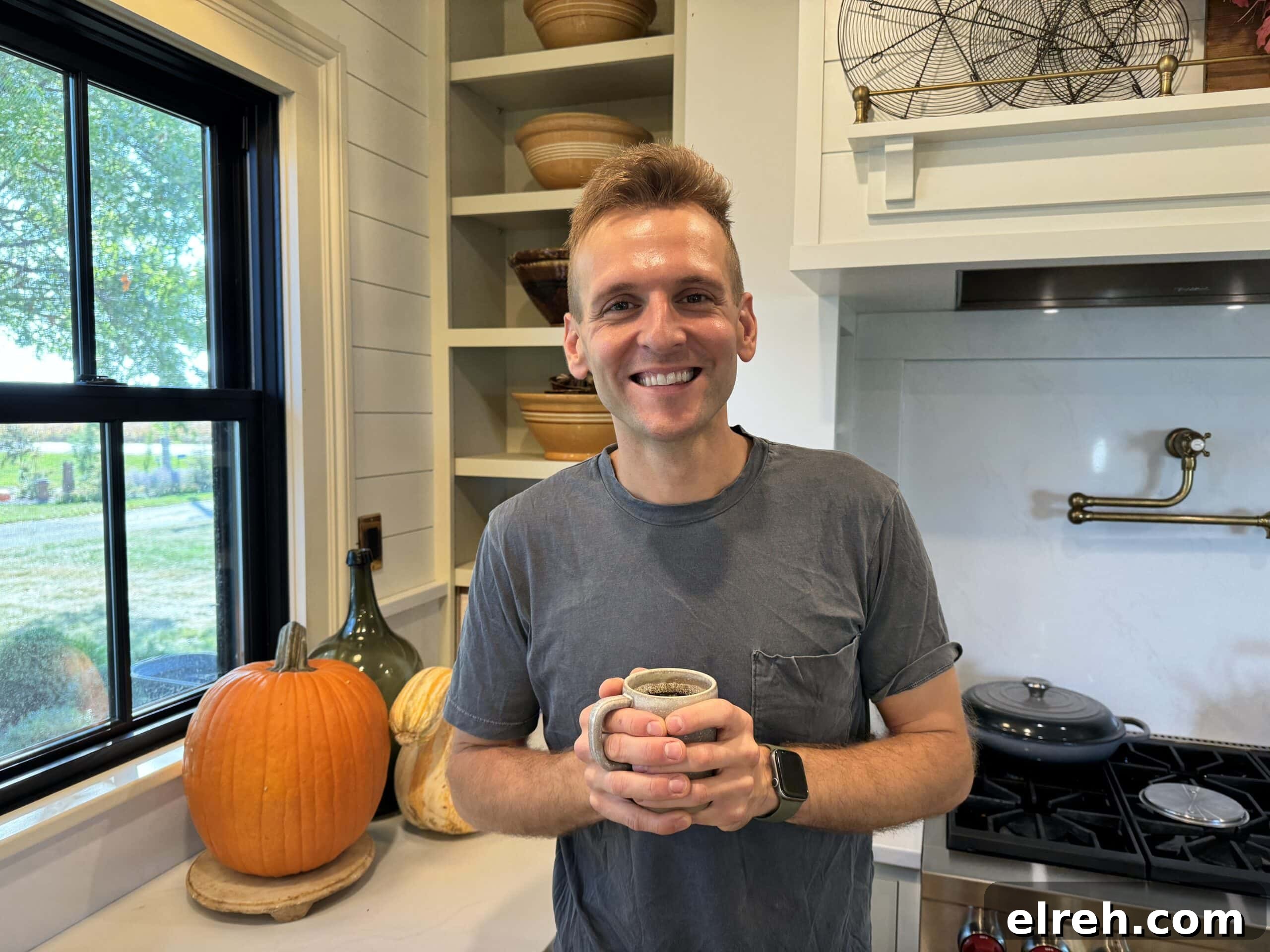 September 2023 Guide to Key Dates Events and Updates 3 Kaleb Wyse standing in kitchen holding a glass of hot coffee with pumpkin in the background.