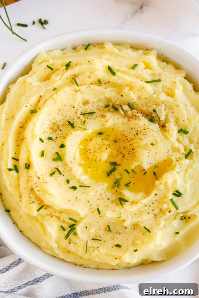 Mashed potatoes in a white bowl topped with butter and chives