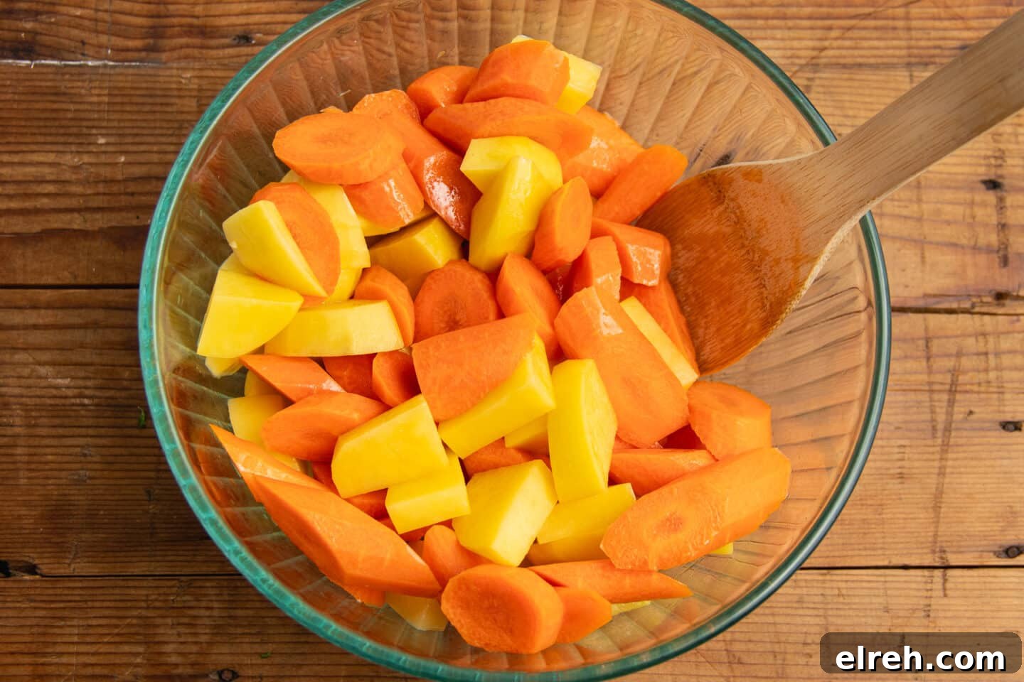 Chopped carrots and potatoes tossed with oil in a bowl.