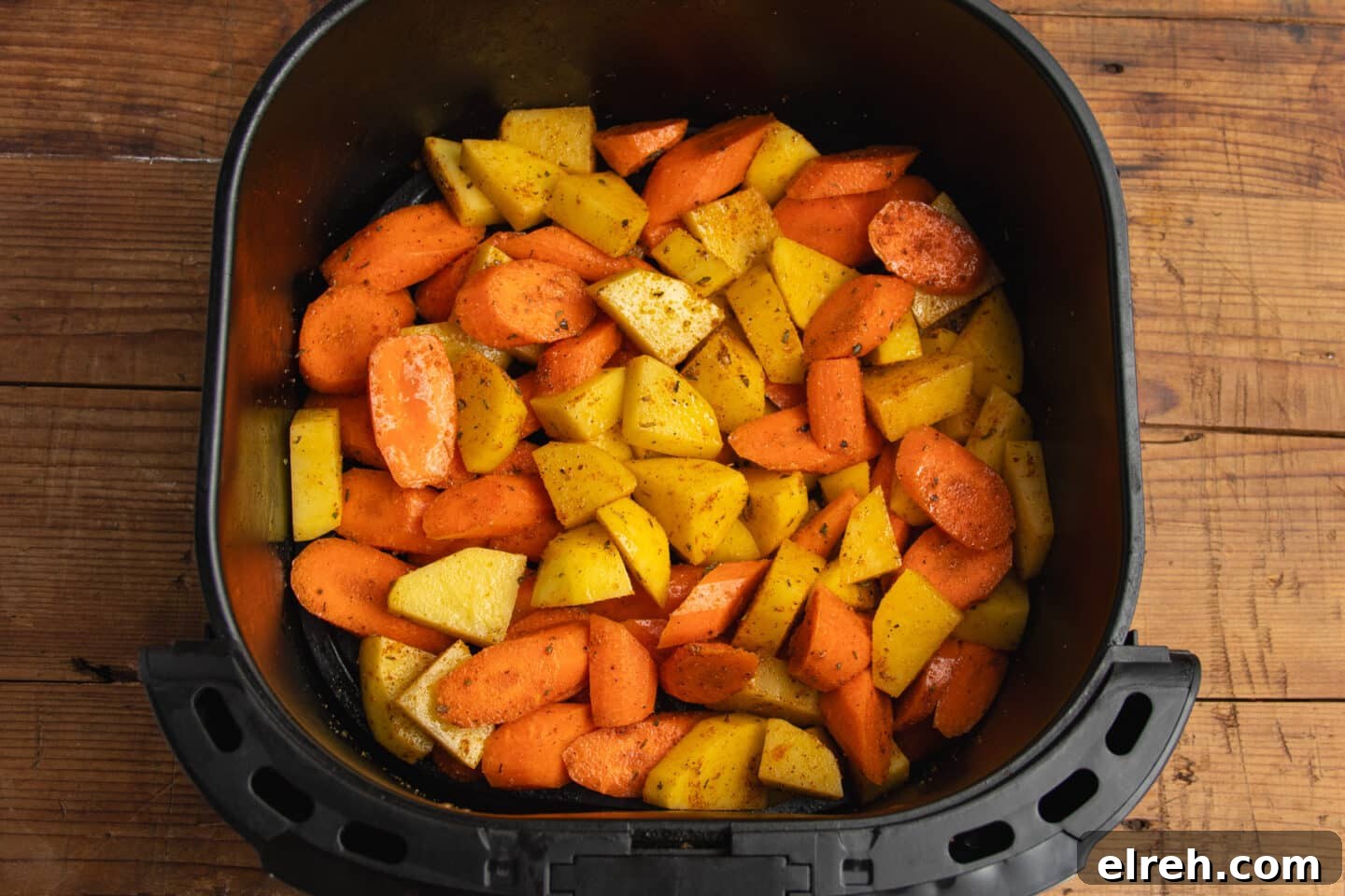 Seasoned carrots and potatoes in an air fryer basket before cooking.