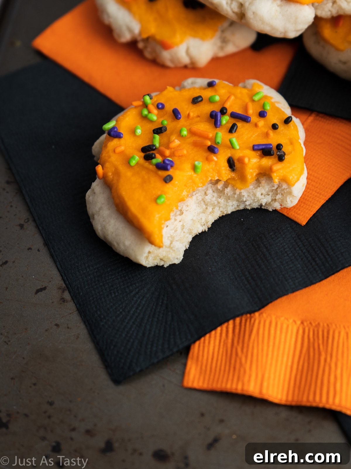 Close-up of an orange frosted sugar cookie with a bite taken out of it.