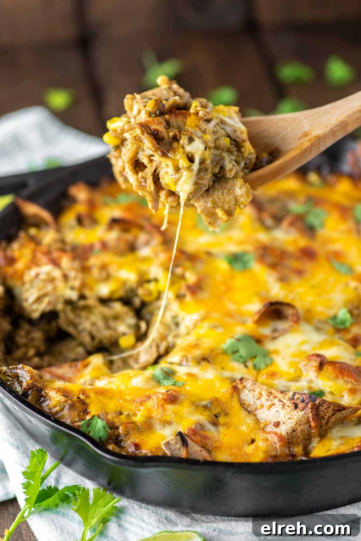 One-Pan Cheesy Chicken Enchilada Skillet 2 Spoon lifting out chicken enchilada skillet in cast iron.