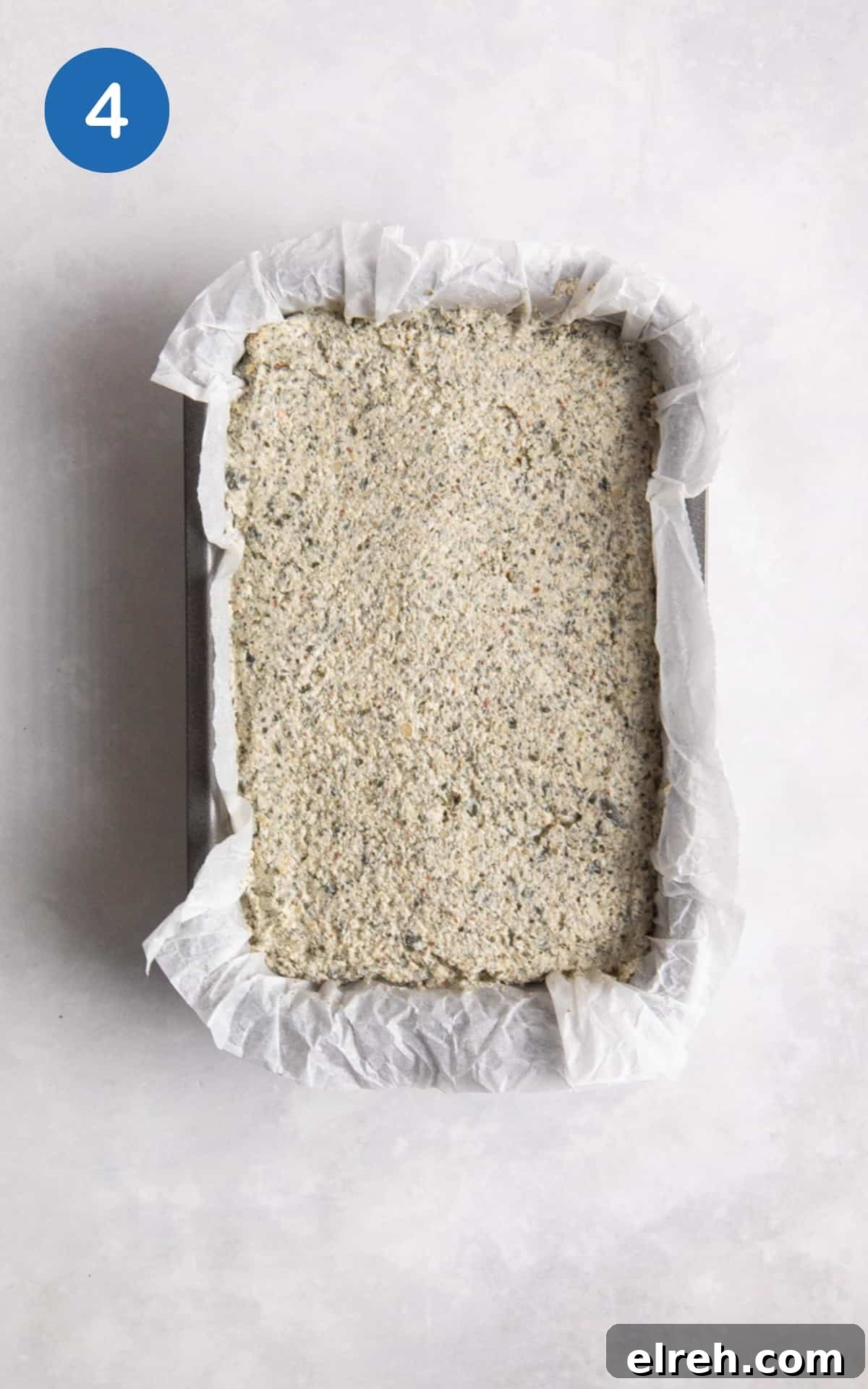 Gluten-Free Seeded Loaf Recipe with Flax, Sunflower and Chia 7 uncooked seeded bread in loaf baking tin with parchment paper on white surface.